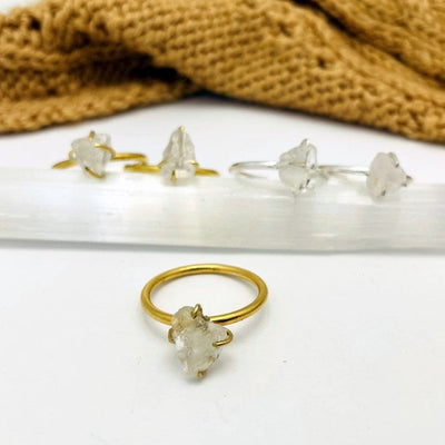 gemstone ring shown on white background with samples of gold and silver in the background