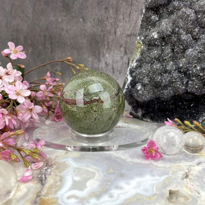 Acrylic Sphere Holder - Clear Oval Holder displayed in an alter holding a sphere decorated with flowers and crystals.