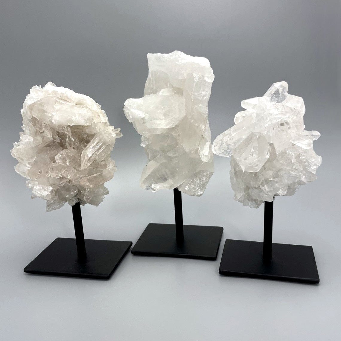 Three Crystal Quartz Cluster on metal stand, displayed on a white surface.