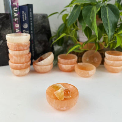 Orange selenite bowls on a table showing color variations with 1 in front with small stones inside