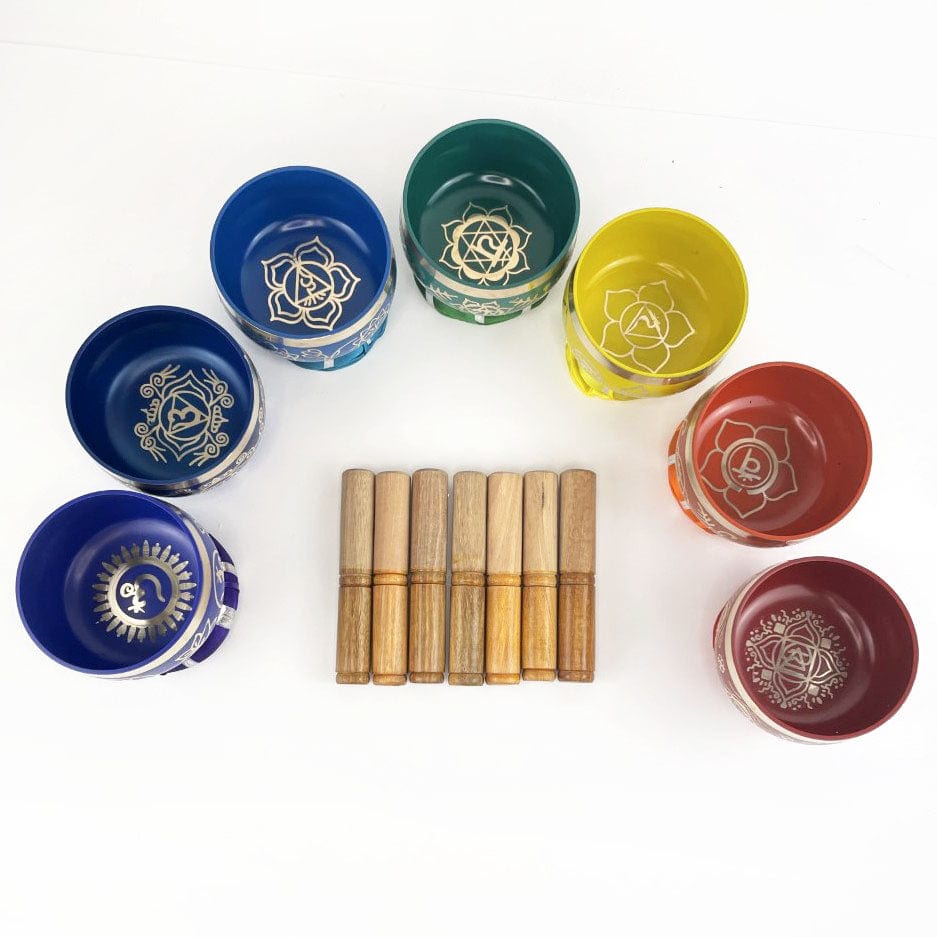 All 7 chakra colorful singing bowls in a semi circle with wooden mallets lined up.