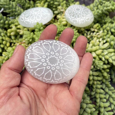 selenite mandala engraved palm stone in hand for size reference with others in background 