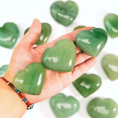 hand holding up 3 Green Aventurine Hearts with others in the background