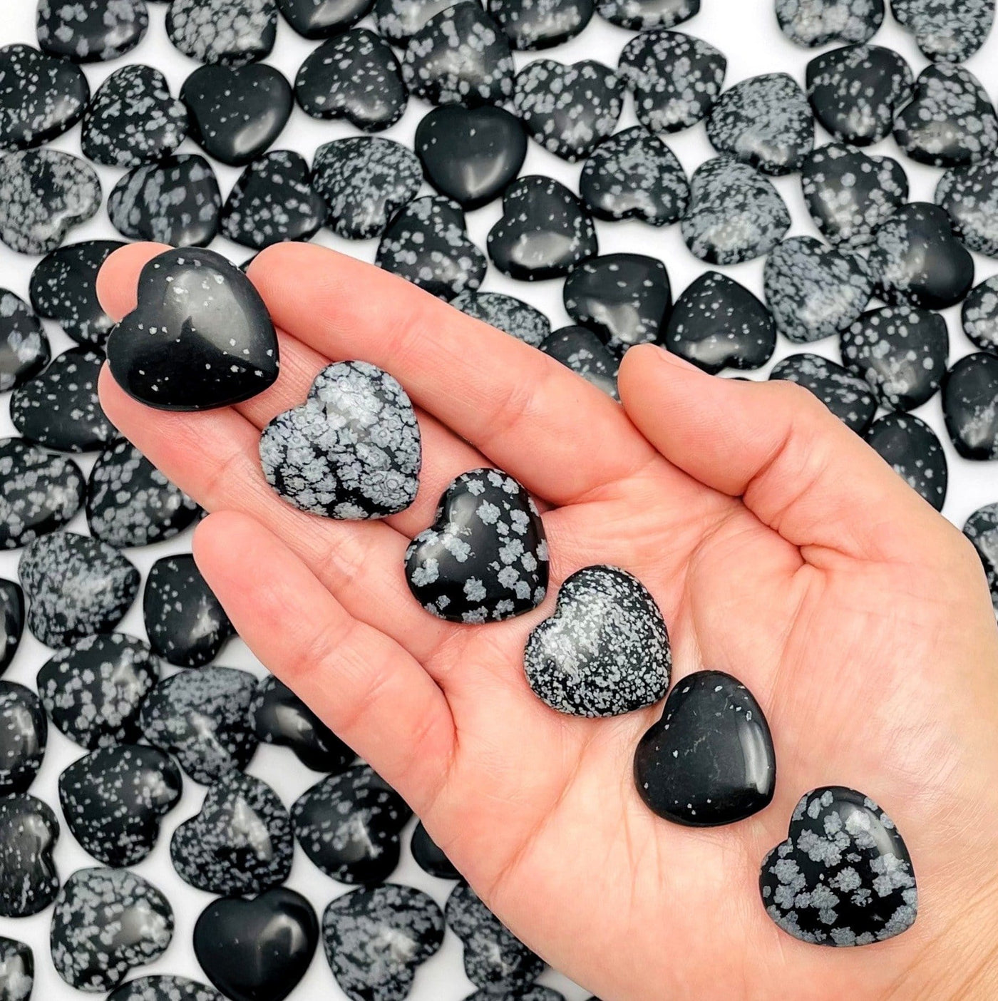 six snowflake obsidian hearts lined up in hand for size reference with many others filling the background for possible variations