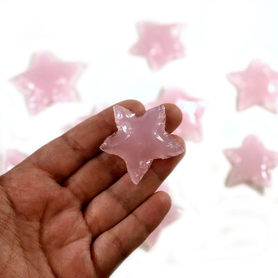 Hand holding up star shaped rose quartz with others blurred in the background
