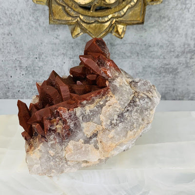 Close up photo of the other side of the red quartz cluster, this picture is also showing the quartz base of the cluster forming slowly into red quartz points on the top of it. red quartz cluster is also being displayed on a white and grey marbled back ground.