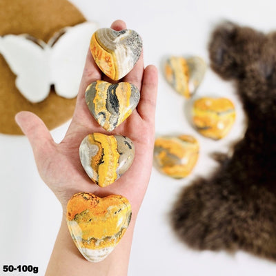 hand holding up 4 50-100g bumblebee jasper hearts with others and decorations blurred in the background