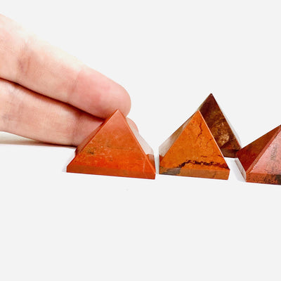 2 fingers behind Red Jasper Pyramid for size reference with 3 others on white background