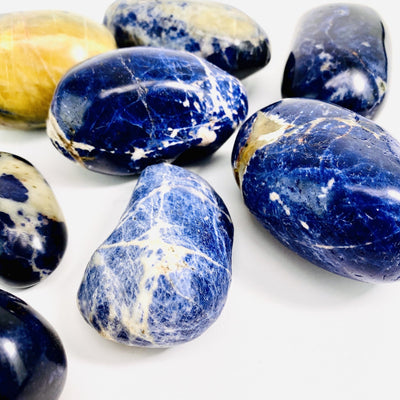 angled close up of many sodalite large tumbled stones on white background for thickness