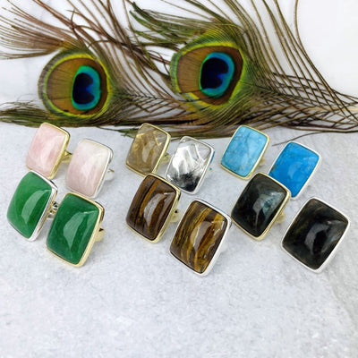 angled view of various stone rings in gold and silver in front of peacock feathers