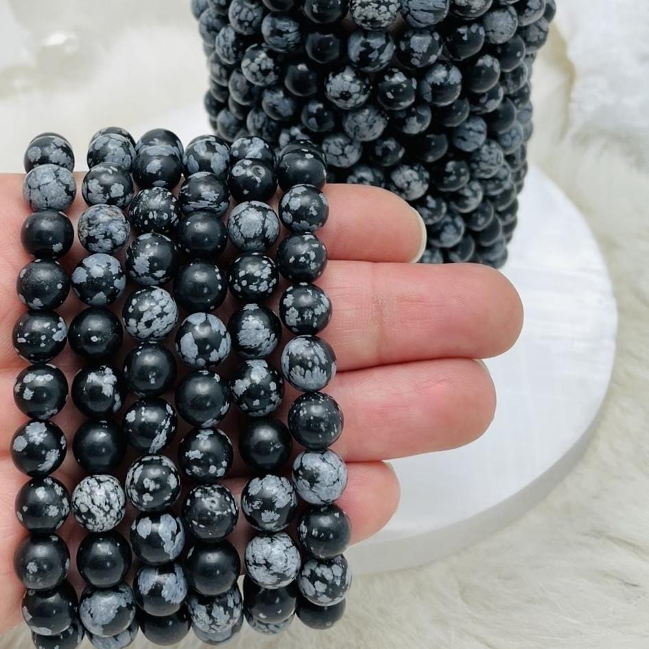 many snowflake jasper round bead bracelets in hand and stacked on background display for size reference and possible variations