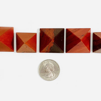 4 Red Jasper Pyramids lined up next to a quarter for size reference on white backround