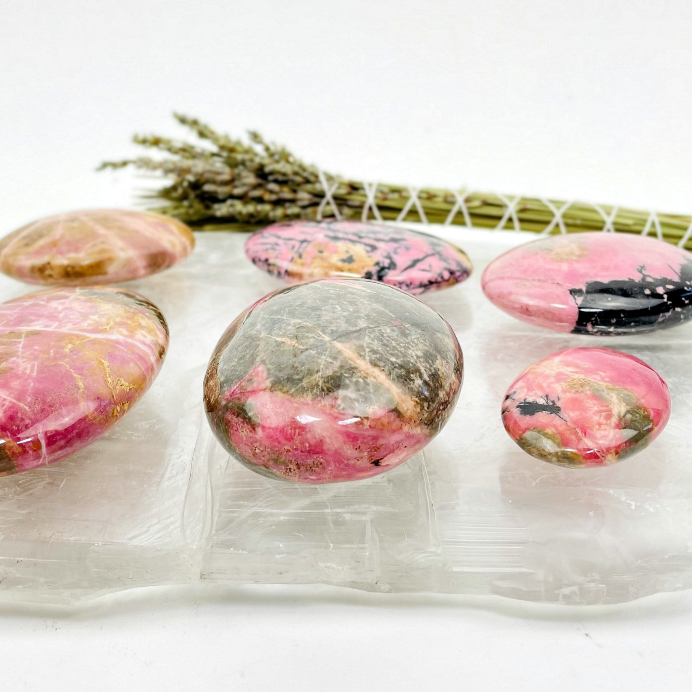 Side view of Rhodonite Palm Stones on top of a selenite slab with a bundle of plants