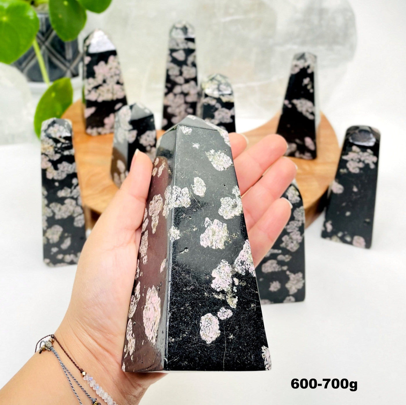 hand holding up 600-700g black jade with pink thulite obelisk with others in the background