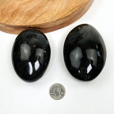 2 obsidian palm stones next to a quarter
