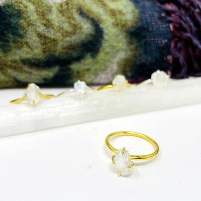 side view of moonstone ring on a white background with 4 others blurred in background on a selenite charging log