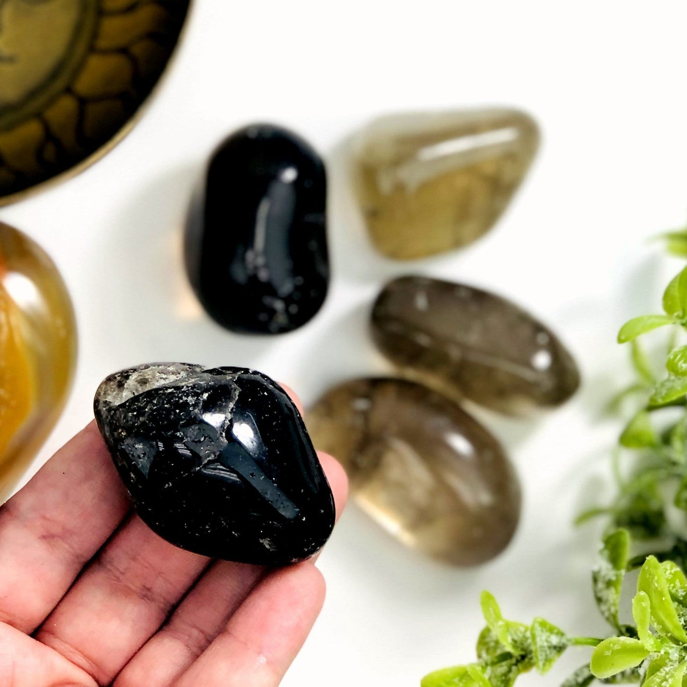 One Black Tumbled Smokey Quartz being lifted by a hand while other stones are out of focus