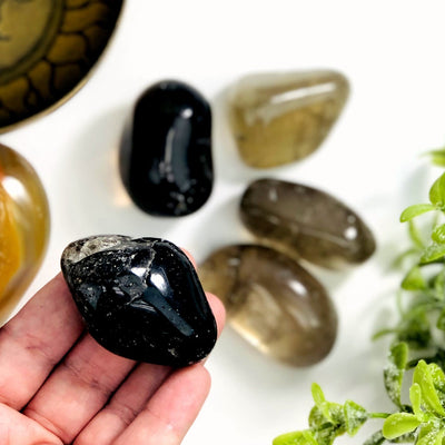 one smokey quartz tumbled gemstone in hand for size reference with four others in background