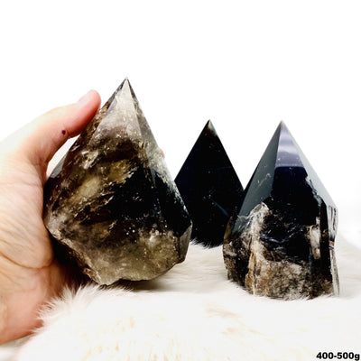 three 400g - 500g smokey quartz semi polished points on display for possible variations with one in hand for size reference