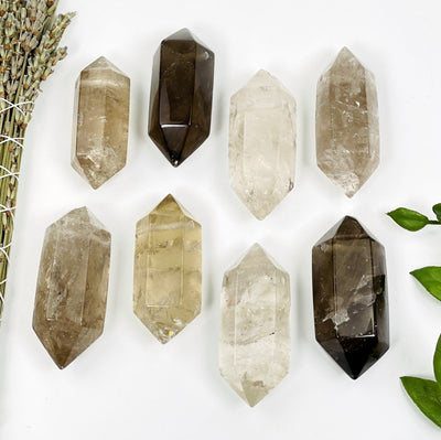 many large drilled smokey quartz double terminated points on white background and plant decorations for possible variations