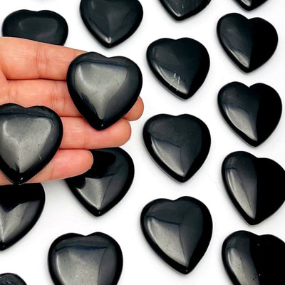 hand holding up 2 Black Obsidian Hearts with others in the background