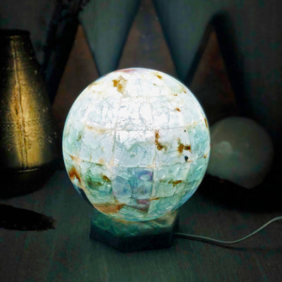 Rainbow Fluorite Sphere Lamp lit up in dark room with various decorations in the background