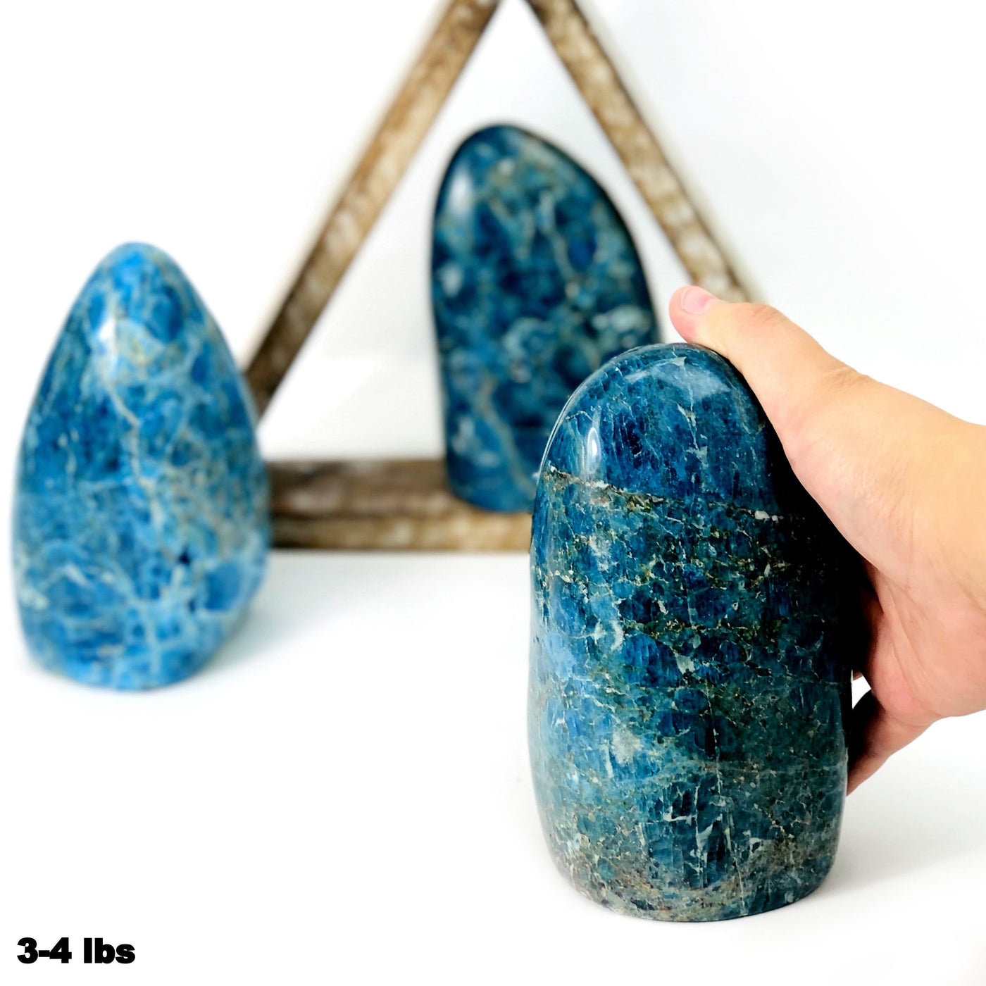 hand holding blue apatite polished cut base in 3-4 lbs with 2 others blurred in the background