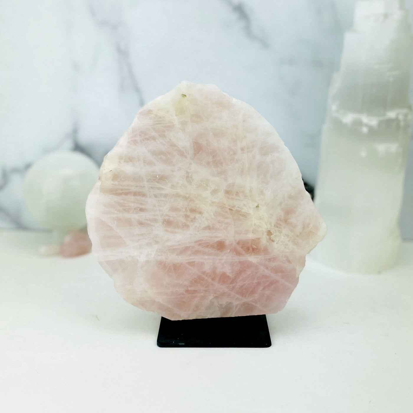 Rose Quartz on Metal Stand with other crystals blurred on marble background