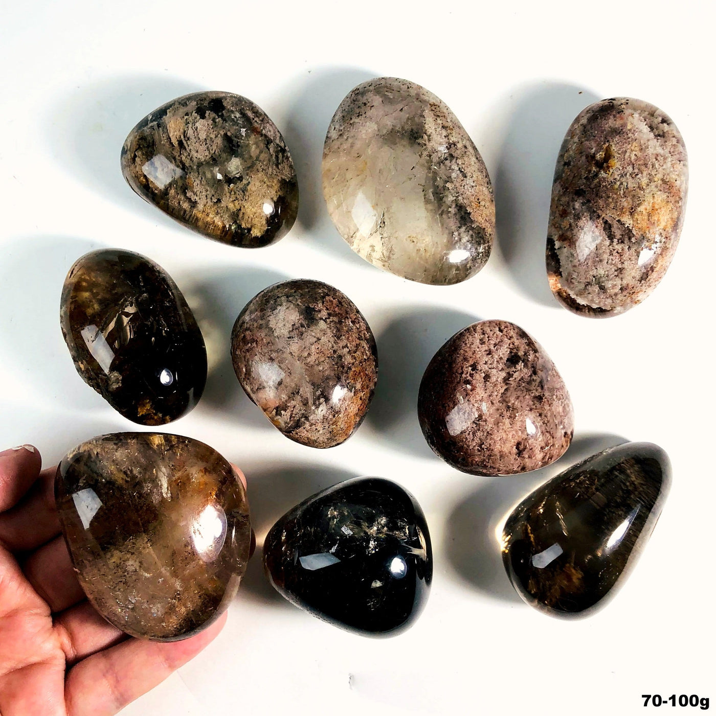 Lodolite tumbled stone assortment on a white background with one held in a man's hand.