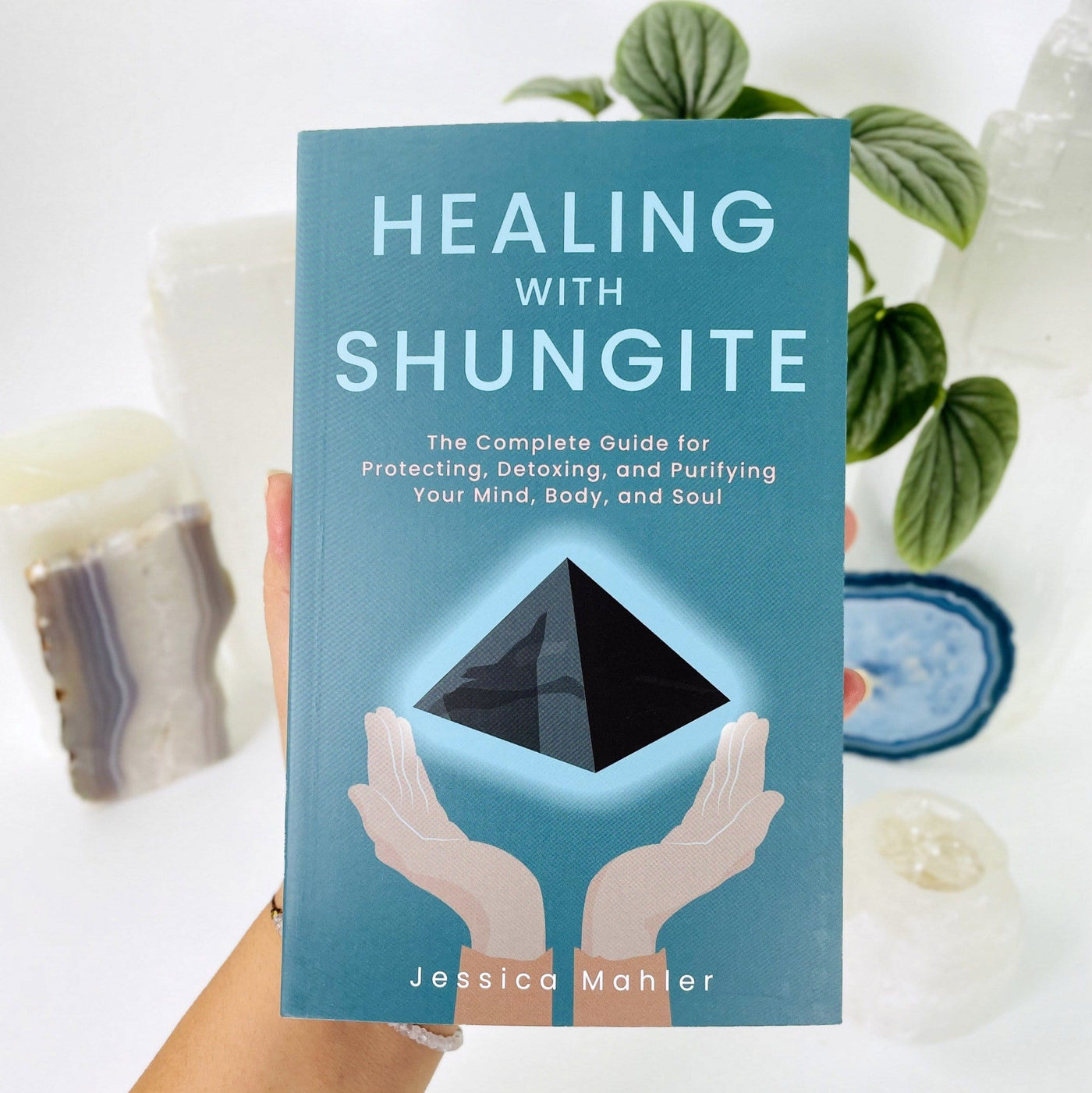 the book healing with shungite being held on a hand to show size and showing the front cover