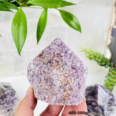 lepidolite semi polished point with decorations in the background