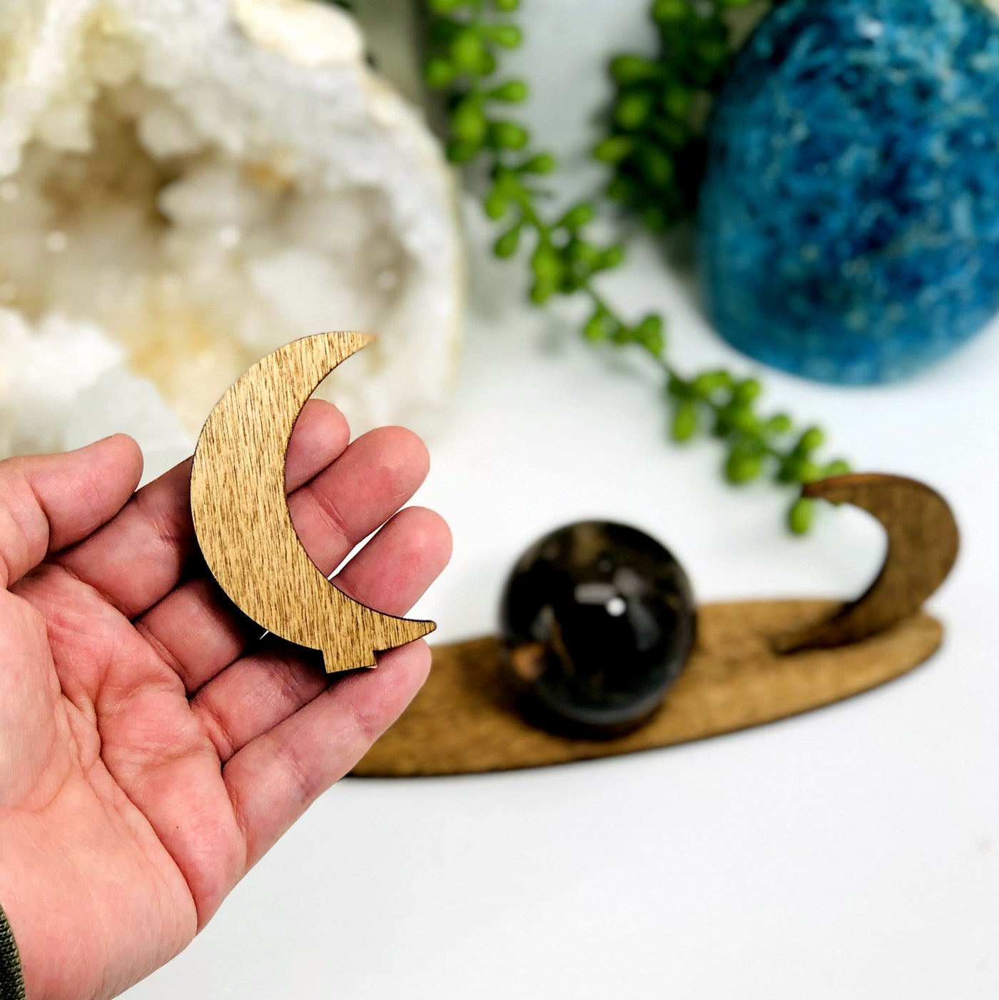 hand holding wooden crescent moon from sphere stand with stand and other crystals blurred in the background