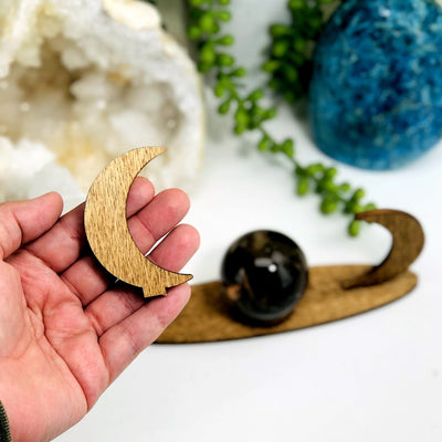 hand holding wooden crescent moon from sphere stand with stand and other crystals blurred in the background