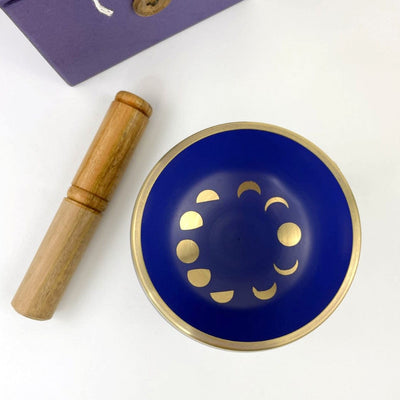 Purple singing bowl with moon phase design from top view, with the box and mallot beside it