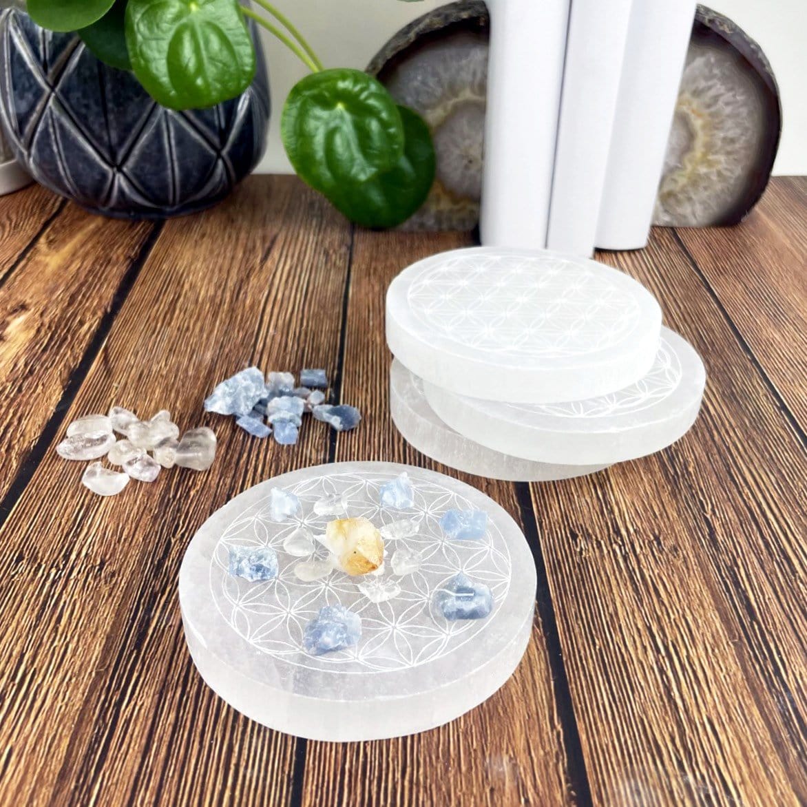 angled view of selenite round plate engraved with flower of life with charging stones and others in background for thickness