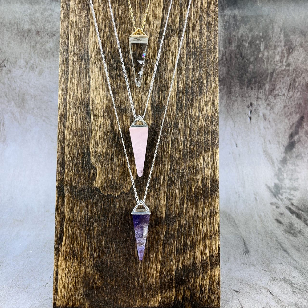 Rose Quartz Amethyst and Crystal Quartz Pendulum Necklaces hanging on a wood bust
