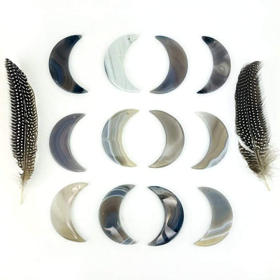Twelve natural agate moons displayed on a white surface next to feathers.