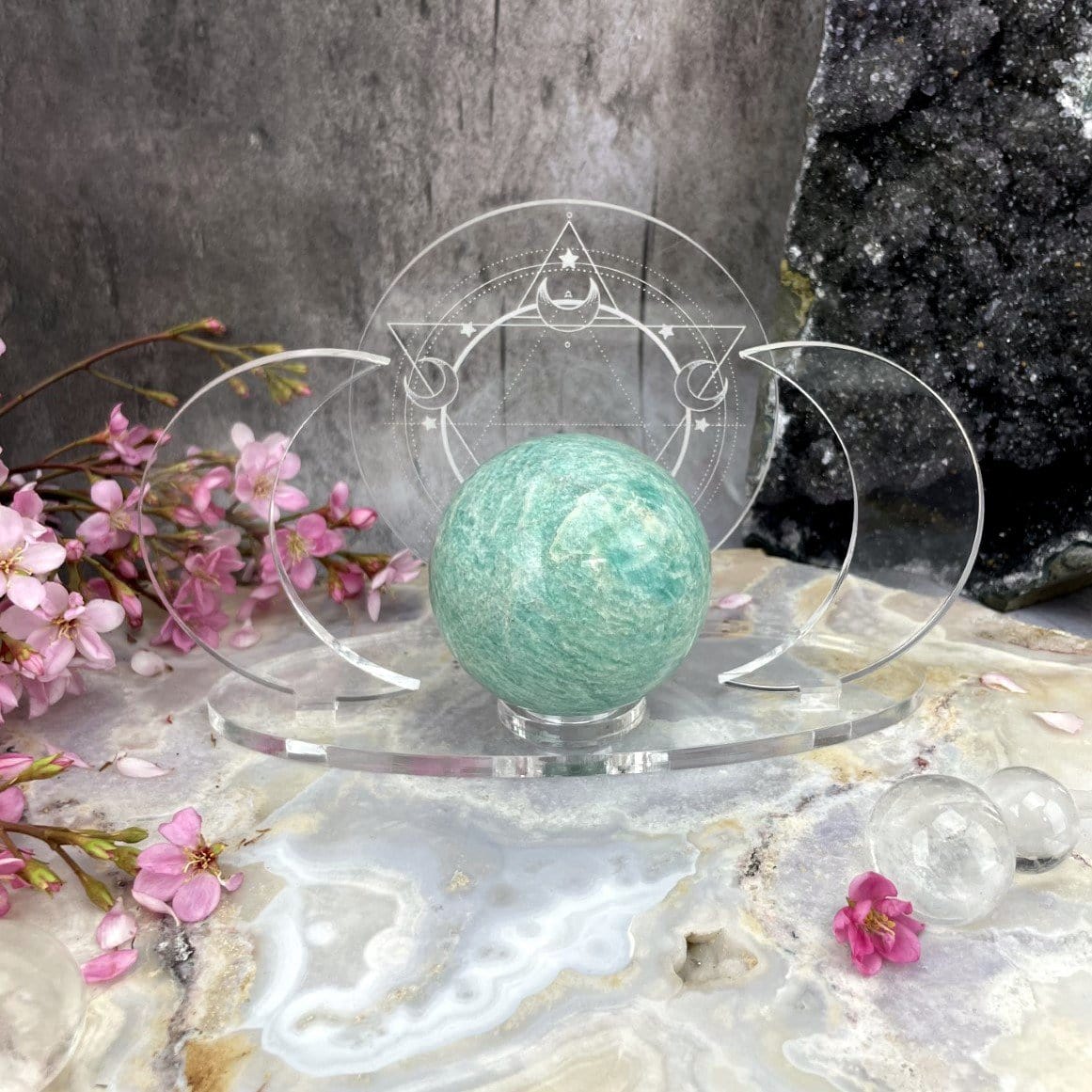 A front facing Acrylic Sphere Holder Crescent Moons - Six Pointed Star in an alter surrounded with flowers and crystals.