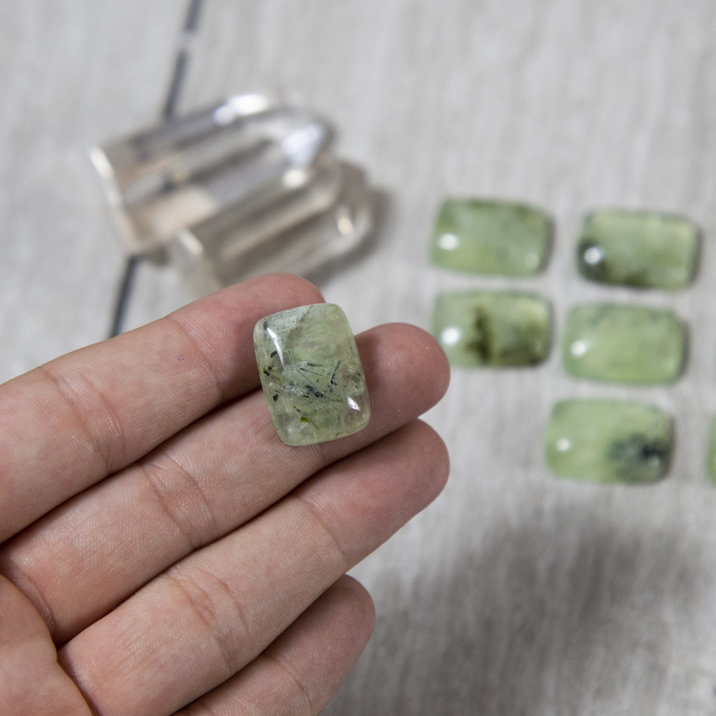 hand holding up prehnite cabochon stone with others blurred in the background