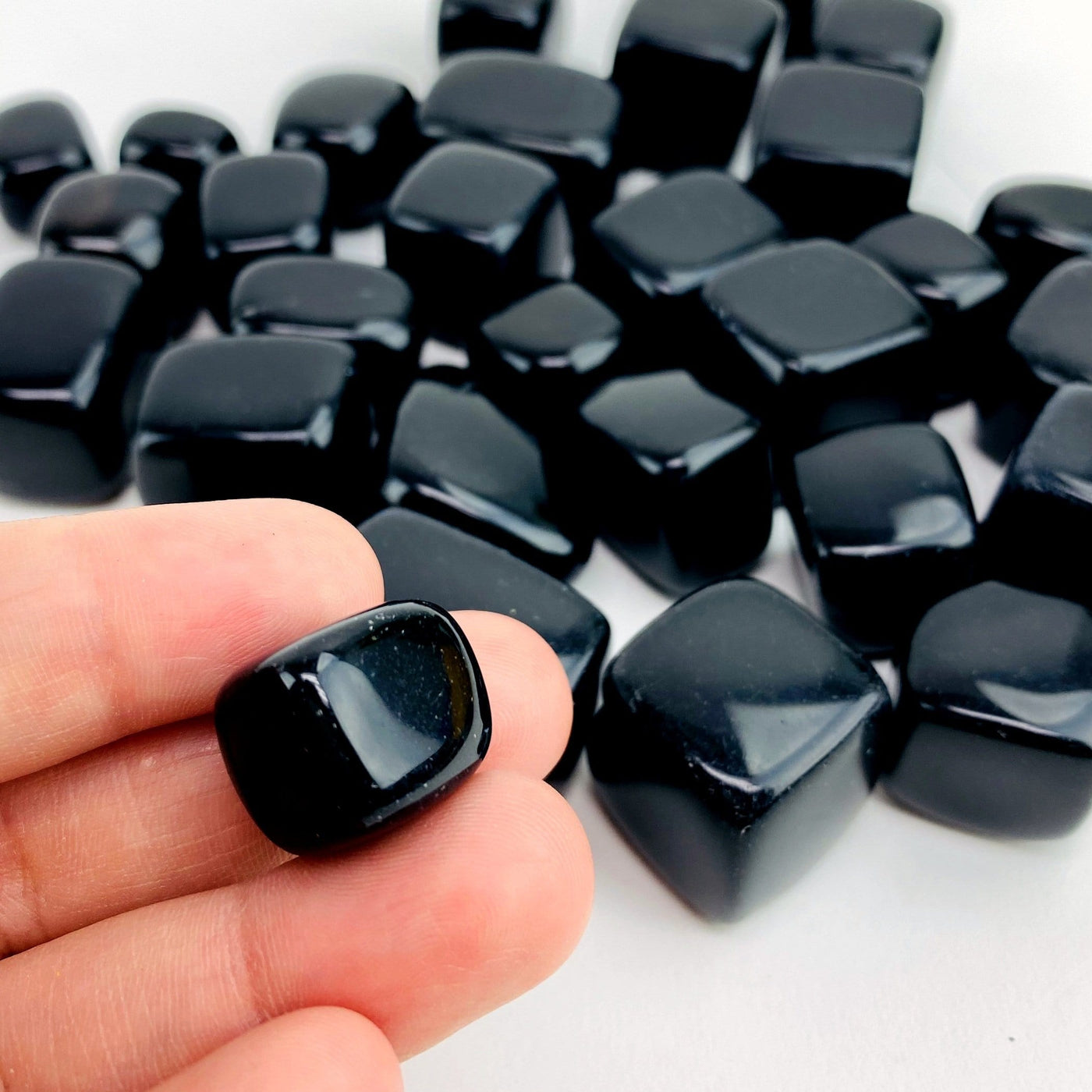 hand holding up obsidian tumbled cube with others in the background