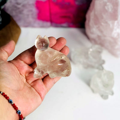 hand holding up Crystal Quartz Cat Mini Statue with decorations in the background