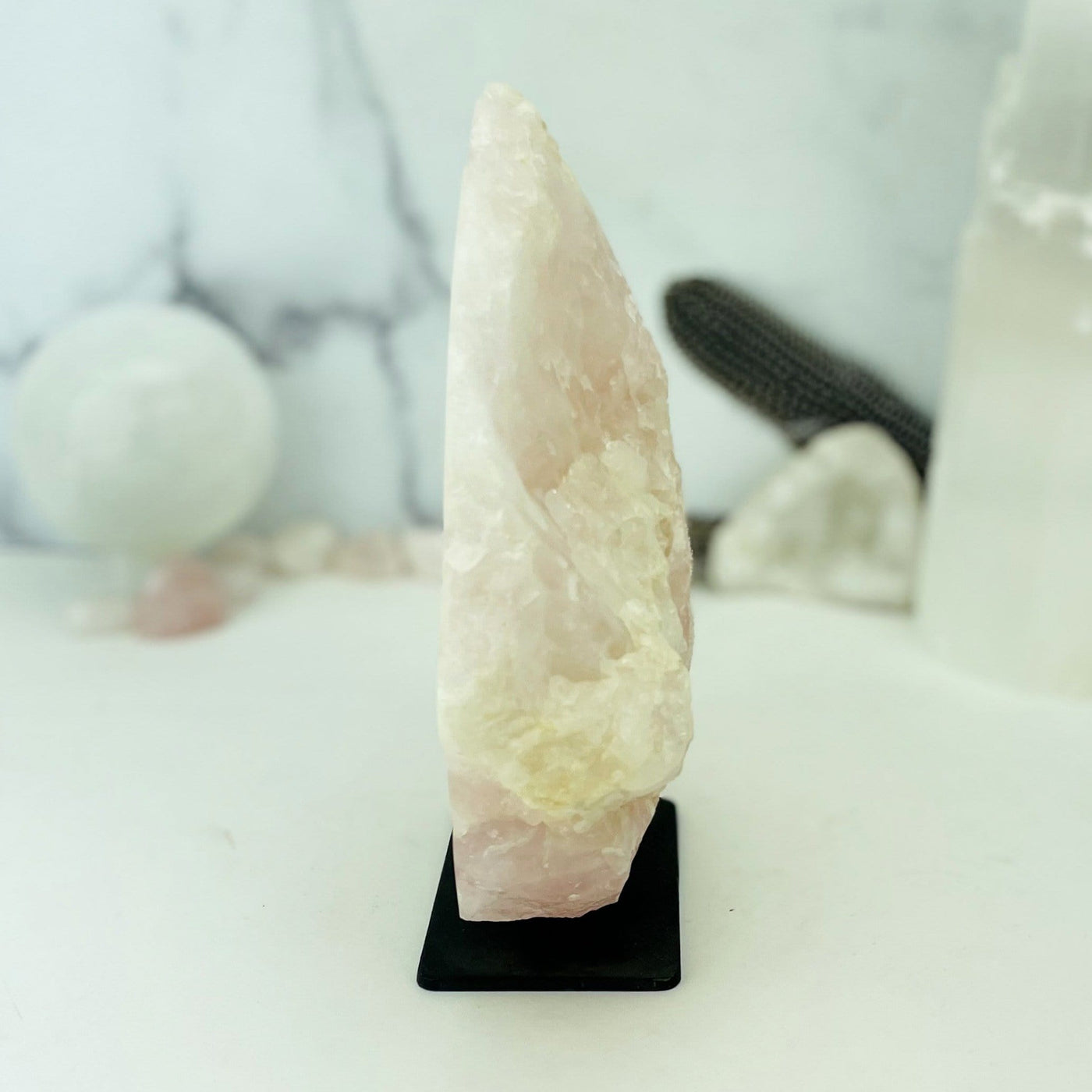 Side view of Rose Quartz on Metal Stand with crystals blurred on marble background