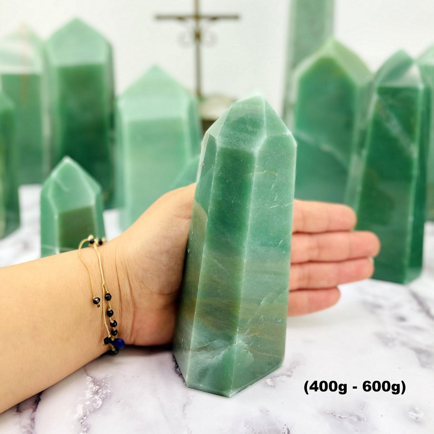 400-600g green quartz tower next to a woman's hand with other green quartz towers in the background.