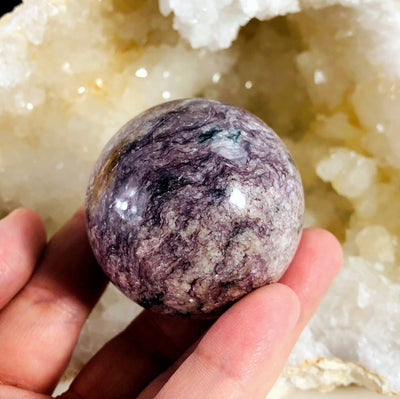 hand holding up Charoite Polished Sphere with decorations in the background