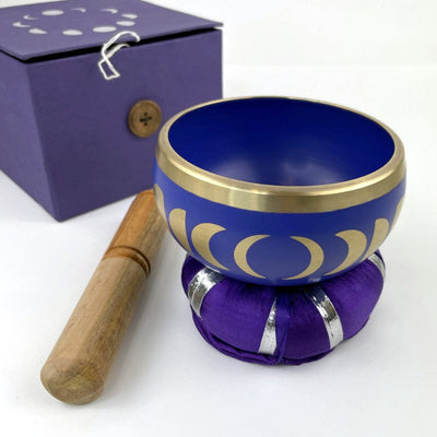 side view of Purple moon phase singing bowl on pillow with mallot and box beside it