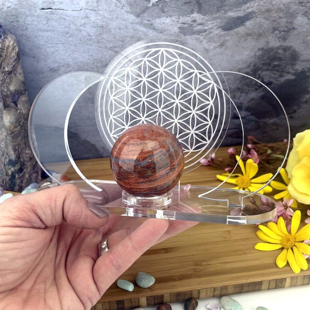 Acrylic Sphere Holder - Crescent Moons with Flower of Life holding a sphere within a hand in an alter with crystals and flowers.
