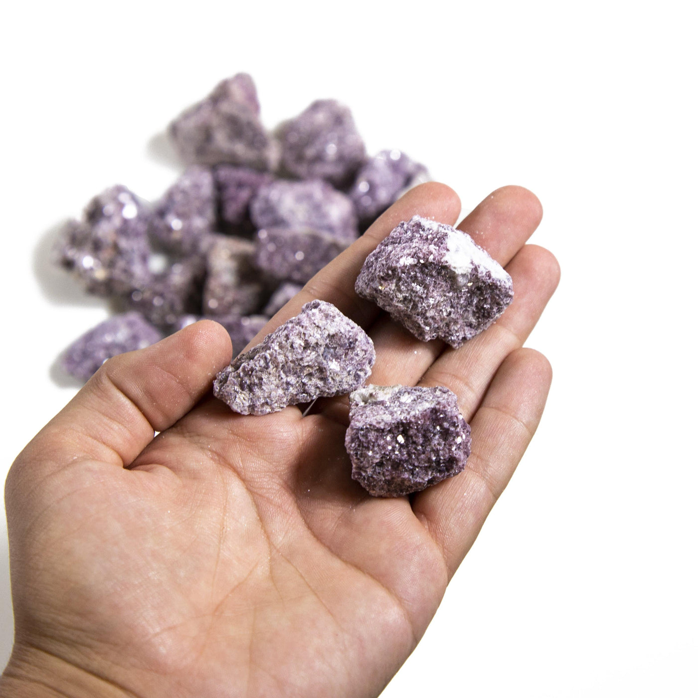 hand holding up 3 Lepidolite Chunks with more blurred in the background
