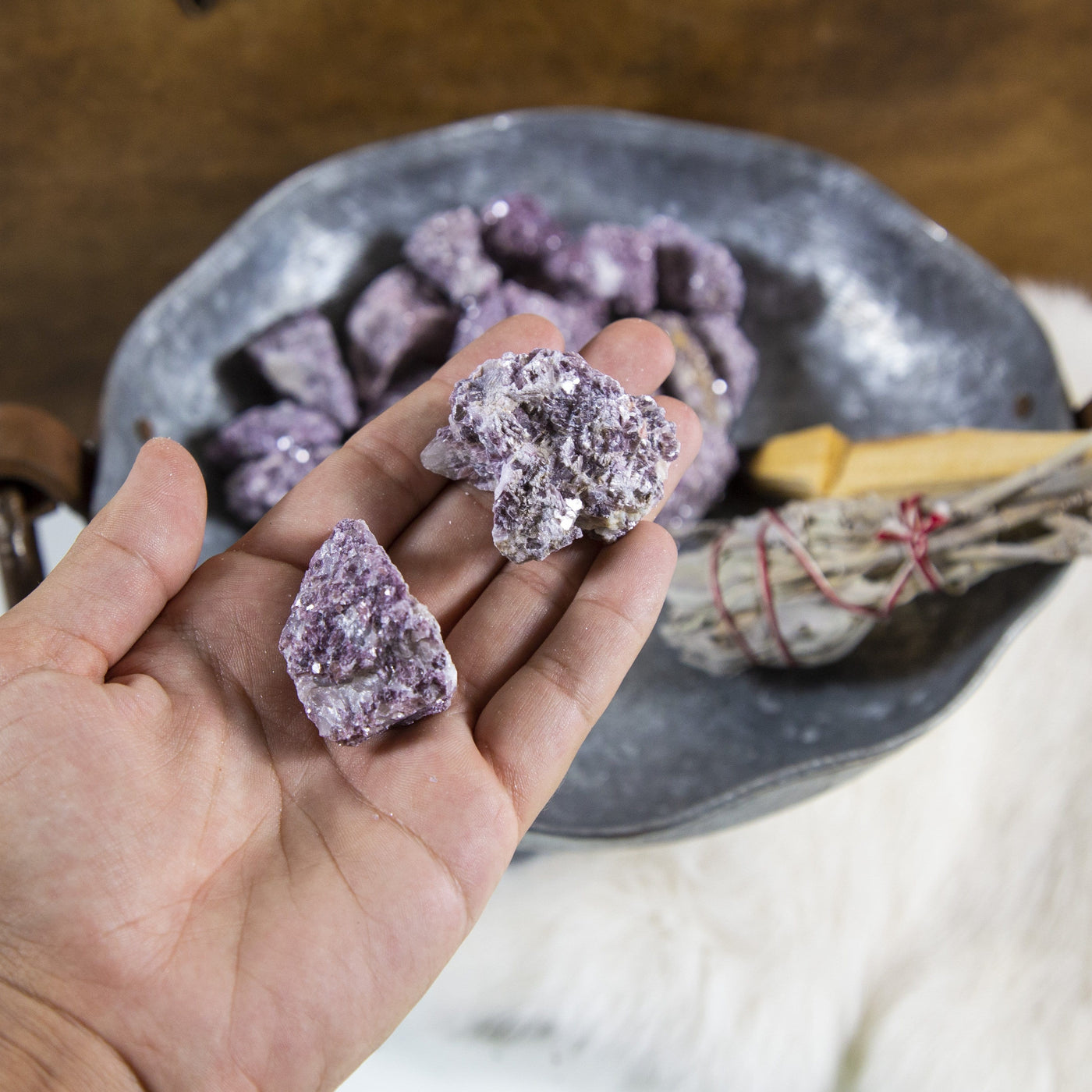 hand holding up 2 Lepidolite Chunks with decorations in the background