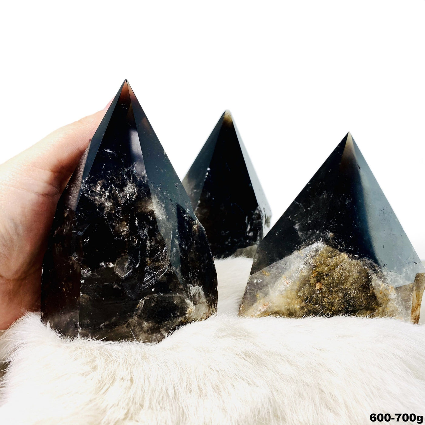 three 600g - 700g smokey quartz semi polished points on display for possible variations with one in hand for size reference