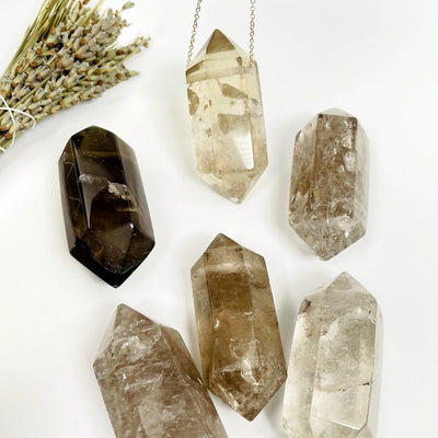 many large drilled smokey quartz double terminated points on white background with plant decorations